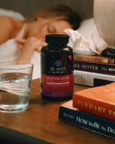 Bottle of Dr. Emil Nutrition Bedtime Burn supplement on a nightstand with books and water glass.