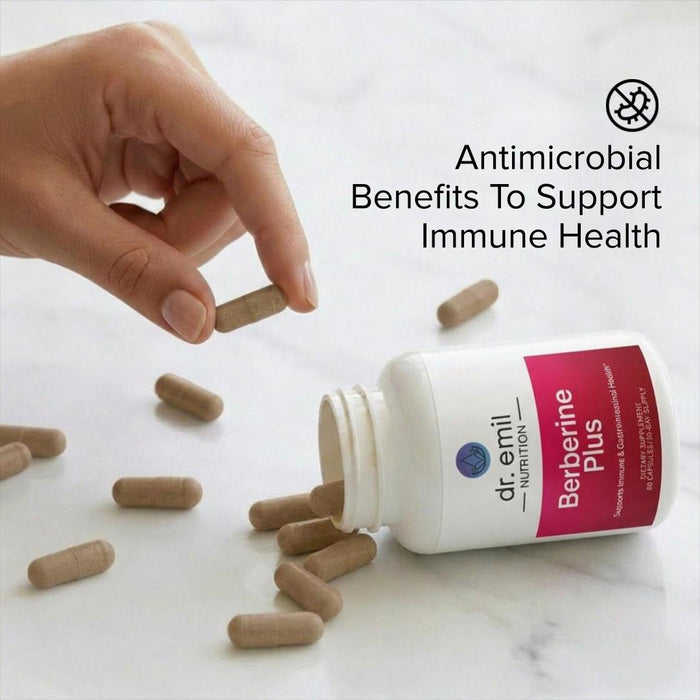 Hand picking a supplement capsule from an open bottle labeled 'Berberine Plus' by dr. emil nutrition on a light background.