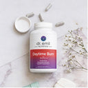 Dr. Emil Nutrition Daytime Burn supplement bottle on a marble surface with capsules and flowers.