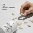 Hand holding a supplement capsule with 'Lions Mane' supplement bottle and scattered capsules on a light background.