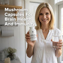 Woman holding a bottle of mushroom capsules and a glass of water in a kitchen.