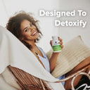 Woman holding a supplement bottle with text 'Designed To Detoxify' in a casual setting.