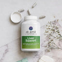 Bottle of dr. emil Nutrition Liver Support supplement on a marble surface with capsules and flowers.