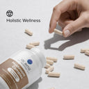 Hand picking a supplement capsule from a bottle labeled 'Holistic Wellness' on a light background.
