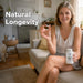 Woman holding a supplement bottle labeled 'NAD' in a home setting with text 'Natural Longevity'.
