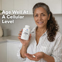 Woman holding a supplement bottle with text 'Age Well At A Cellular Level' in a kitchen setting.