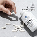 Hand holding a supplement pill next to a bottle labeled 'NMN' with text about supporting healthy aging.