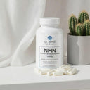 Dr. Emil Nutrition NMN supplement bottle with capsules on a white surface next to a cactus plant.