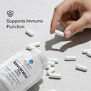 Hand picking up a Resveratrol supplement capsule with a bottle of supplements on a light background.