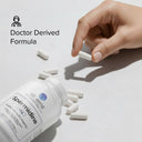 Hand picking up a supplement capsule from a bottle labeled 'dr. emil spermidine' on a light background.