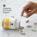 Hand pouring supplements from a bottle labeled 'Complete Gut Health Support' on a marble surface.
