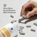 Hand holding a probiotic supplement bottle with scattered capsules on a light background.