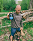 Man holding a 5-HTP supplement bottle with a dog in a natural setting