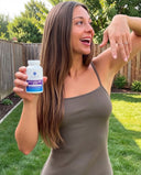 Woman holding a Multi Collagen Plus Biotin supplement bottle outdoors with a wooden fence and greenery in the background